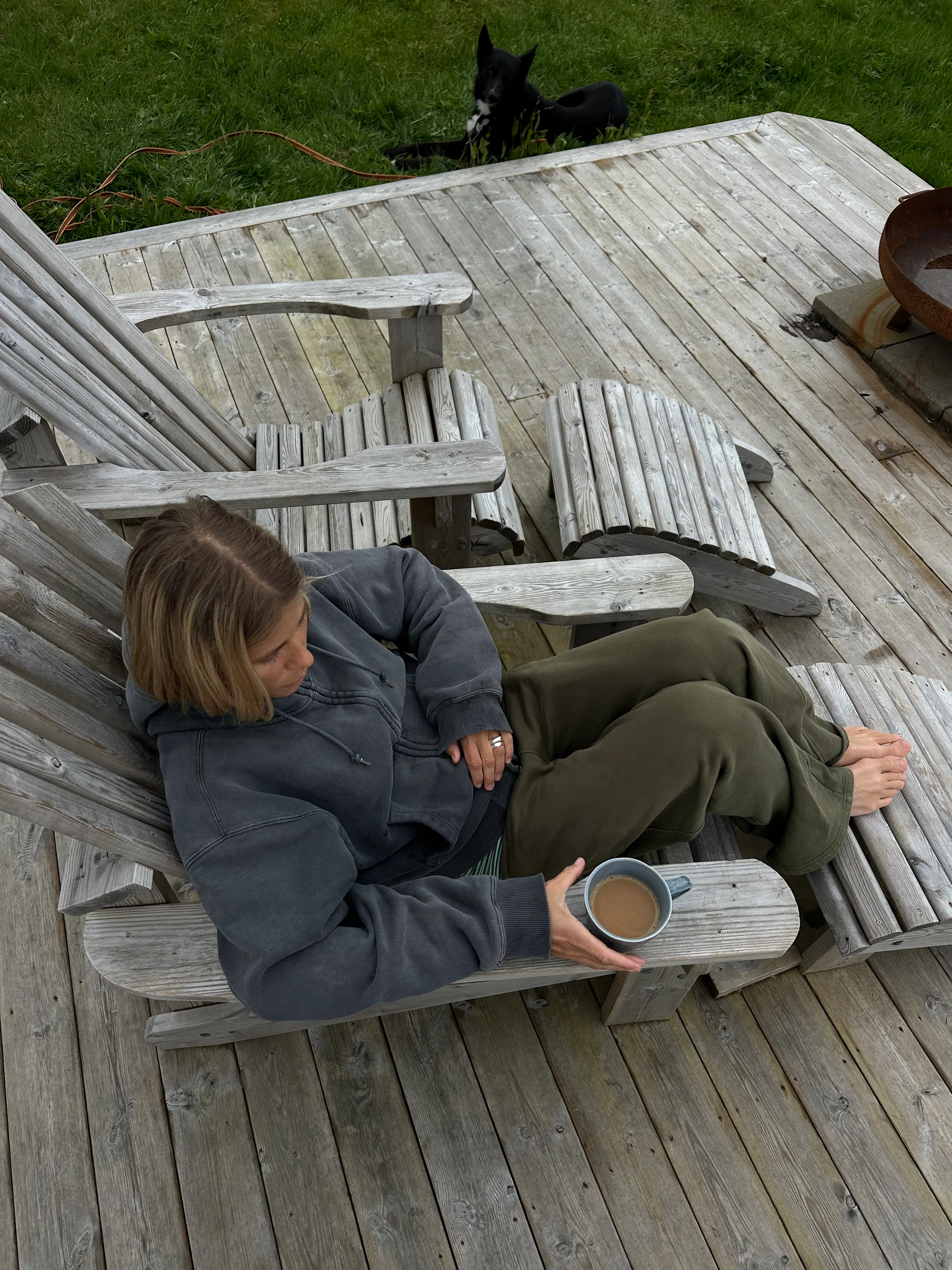 Agnes sitting on the wooden deck with coffee and a book during the Lofoten stay